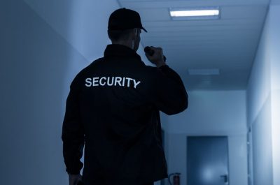 A security guard patrolling a dimly lit hallway at night.